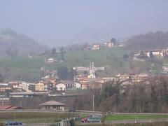 A scenic view of Vertova in Bergamo, Italy with traditional stone houses against a mountainous backdrop.