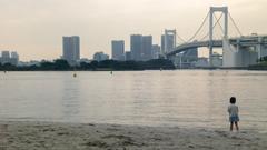 little girl looking at the Rainbow Bridge in Odaiba beach at sunset