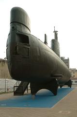 Cylindrical submarine hull with blue-green upper part and matte black lower part, with wave-breaking bow and tapered stern resembling a drop shape