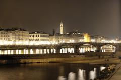 the cityscape of Florence at night with a prominent tower and bridge illuminated by lights