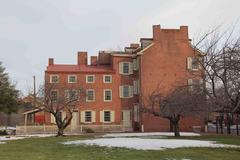 a brick house with wooden shutters surrounded by a grassy field with snow patches and trees