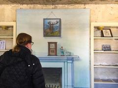 visitor at Edgar Allan Poe National Historic Site viewing painting of a fireplace and nearly empty bookshelf