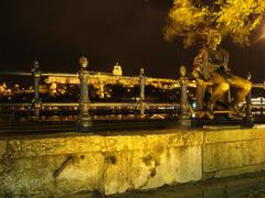 Little Princess statue at nighttime with a view of the Danube and Castle Hill in Budapest, Hungary