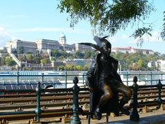 Estátua de bronze de um menino segurando um peixe, com o palácio real ao fundo