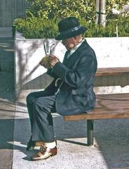 A man with an umbrella cleaning his glasses in a park