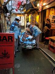 elderly man attended by firefighters on a gurney in Omoide-Yokocho, Shinjuku, Tokyo