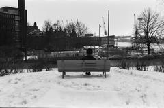 Man sitting on a bench in snowy Katajanokan puisto (Tove Janssonin puisto) with view towards Eteläsatama, Helsinki, 1972