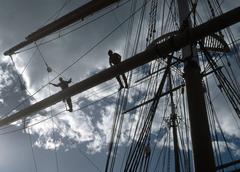 Park rangers on a foot rope above a sailing ship's deck