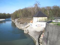 Isar river below the weir with the operating building of the new underground power plant, old and unfinished fish ladder ending at the wooden wall, and power plant outlet below the operating building