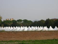 A group of white gazebos arranged for an event, visible through a hole in a brick wall