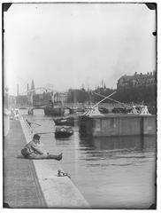 Historical photograph of Amstel 51-55, boy by the canal, view towards Amstelsluizen and Magere Brug