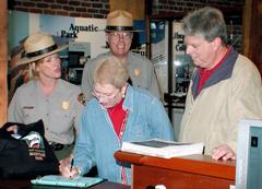 A woman signing a guest book at a visitor center while three others observe.