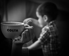 A black and white photo of a person offering a cup of tea on the street