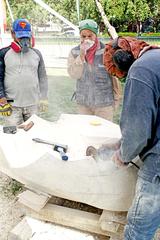 sculptor works on a large stone sculpture outdoors