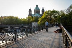 View of the Münchner Kabelsteg bridge over Kleine Isar with Art Nouveau railing, Wehrsteg bridge on the left, and St. Lukas Church in the background