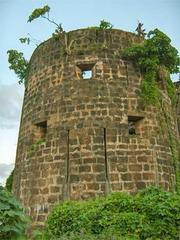 A distant view of Madh Fort with greenery in the foreground