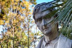 three quarter front view of a pensive sculpture amidst foliage