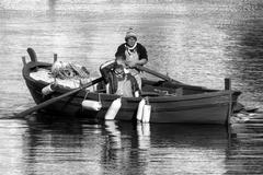 Side view of a person rowing a boat near a pier on a calm river