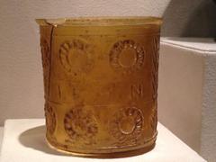 Amber-colored cylinder-shaped glass vessel with Greek inscription and wreaths