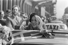 Melina Mercouri arrives at Amsterdam Central Station wearing a beret and holding a Greek flag