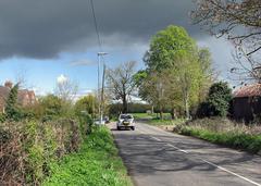 A bend in Granham's Road with grassy fields and cloudy sky