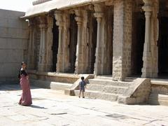 Mother and child wander through courtyard flanked by columns in Hampi