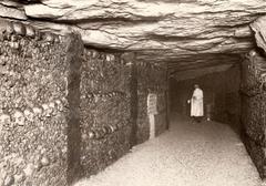 Guide with a cap and collection box in a corridor of the Paris Catacombs, walls covered with skulls, France, 1929