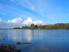 Castle in Menlough, Galway with clouds, river, and mountains in the background