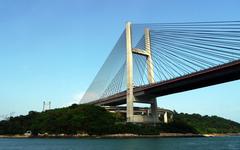 Bridge spanning Hong Kong harbor at dusk with city skyline in the background