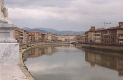 view of Arno River in Pisa with historic buildings and mountains in the background