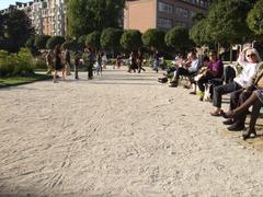 People gathered around a large sandbox with buildings in the background