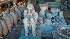 Cast of a man crouched in a corner with a scarf over his mouth in Pompeii