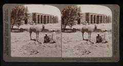 Camel and two people in foreground; man on donkey in front of temple at Thebes, Egypt