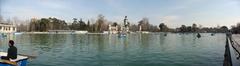 A scenic view of El Retiro Park with a lake, trees, and a monument on a sunny day