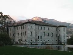 A photo of Trento's Le Albere district with modern buildings, green spaces, and mountainous backdrop.