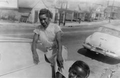 Delois Marie JOHNSON poses on a 1953 Pontiac convertible with a child partially visible in foreground on South Street, Raleigh, NC, 1956-1957