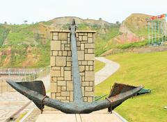 Large anchor displayed on grass with a coastline in the background