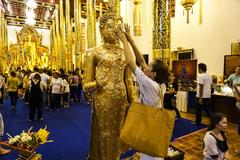 Buddhist follower pressing gold leaf onto a Buddha image at Wat Chedi Luang on Visakha Bucha Day