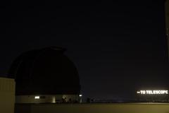 Griffith Park Observatory at night with a telescope in the foreground