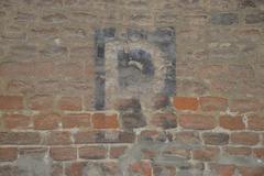 A large letter 'R' on the exterior wall of the Archbishop's palace in Novara indicating the presence of a World War II air raid shelter