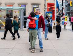 A person with 'Hug Me' poster being hugged by another person on Dundas Square in Toronto