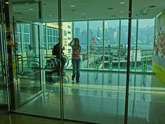 Harbour City glass lobby interior with visitors viewing Victoria Harbour