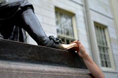 Visitor rubs the left foot of John Harvard statue for good luck at Harvard University