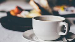 A cup of coffee on a wooden table with a notebook and pen beside it