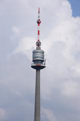 Donauturm tower in Vienna against a blue sky with trees in the foreground