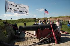 Historic reenactors behind a cannon at Fort McHenry with flag reading 'A free trade and sailors rights'