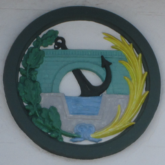 Escudo del Colegio de Ingenieros de Caminos, Canales y Puertos esculpido en el edificio de la Junta de Obras del Puerto de San Esteban de Pravia