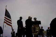 Men talking behind microphone podium on stage with NPS employees at Carlsbad National Monument