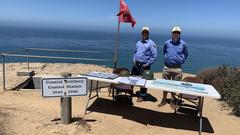 Military History volunteers standing by Coastal Artillery Control Station sign with sandstone cliffs and Pacific Ocean in background