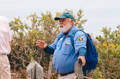 Park Rover volunteer in Volunteers-In-Parks uniform assisting visitor near yellow bladderpod bush